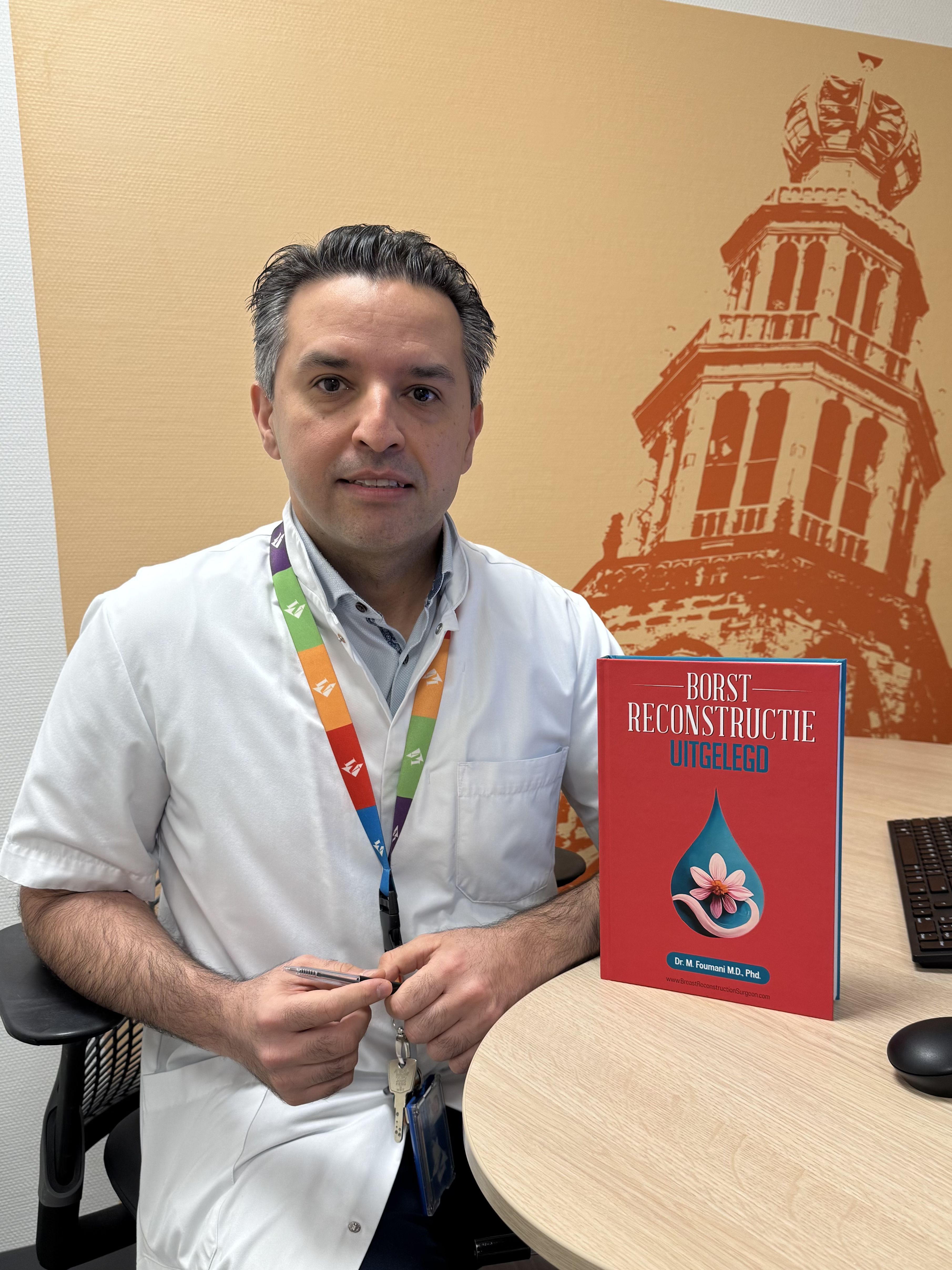 Plastisch chirurg Mahyar Foumani zit in de spreekkamer met zijn boek 'borstreconstructie uitgelegd' Plastisch chirurg Mahyar Foumani zit in de spreekkamer met zijn boek 'borstreconstructie uitgelegd'